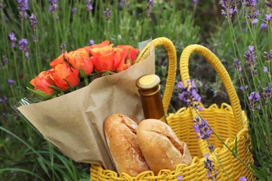 Photo of Yellow wicker bag with beautiful roses, bottle of wine and baguettes in lavender field, closeup