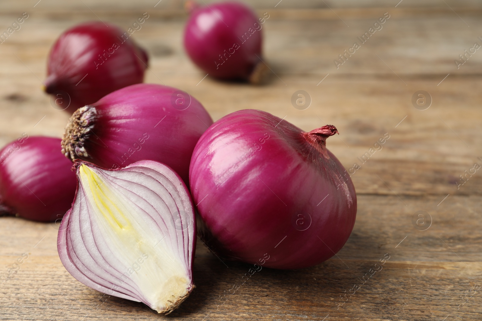 Photo of Ripe red onion bulbs on wooden table, closeup