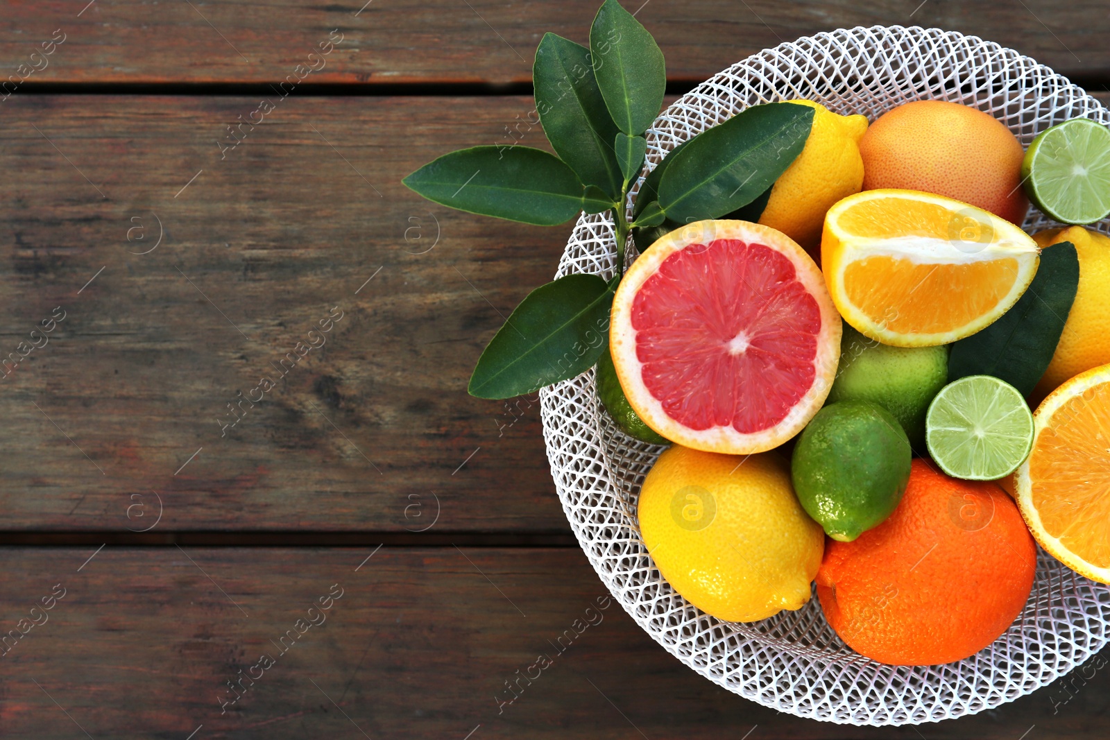 Photo of Bowl with different citrus fruits and leaves on wooden table, top view. Space for text