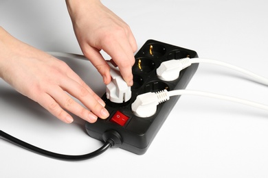 Woman putting plug into extension cord on white background, closeup. Electrician's equipment