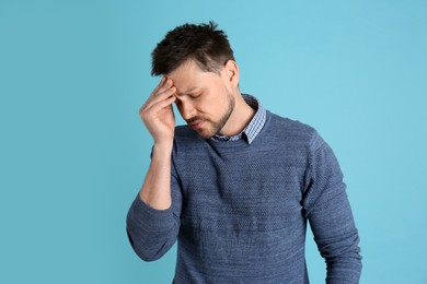 Photo of Man suffering from terrible migraine on light blue background