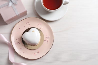 Photo of St. Valentine's Day. Delicious heart shaped cake, tea and gift on white wooden table, flat lay. Space for text