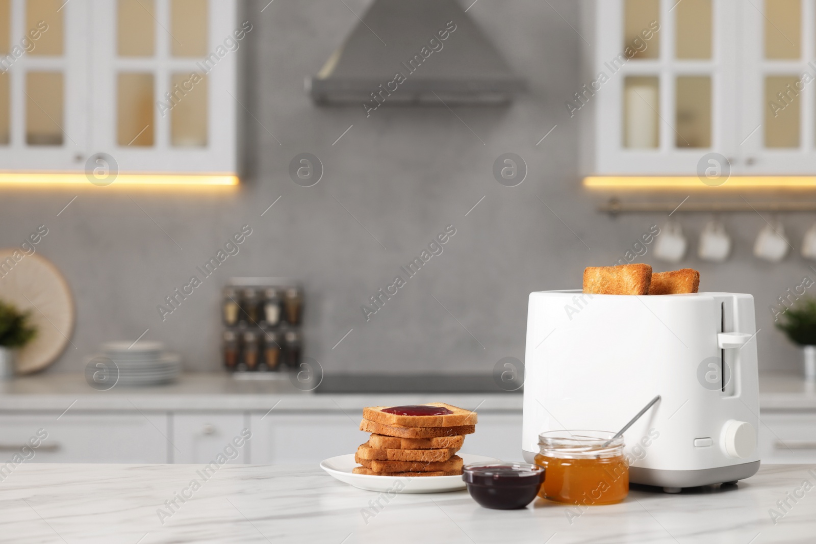 Photo of Making toasts for breakfast. Appliance, crunchy bread, honey and jam on white table in kitchen. Space for text