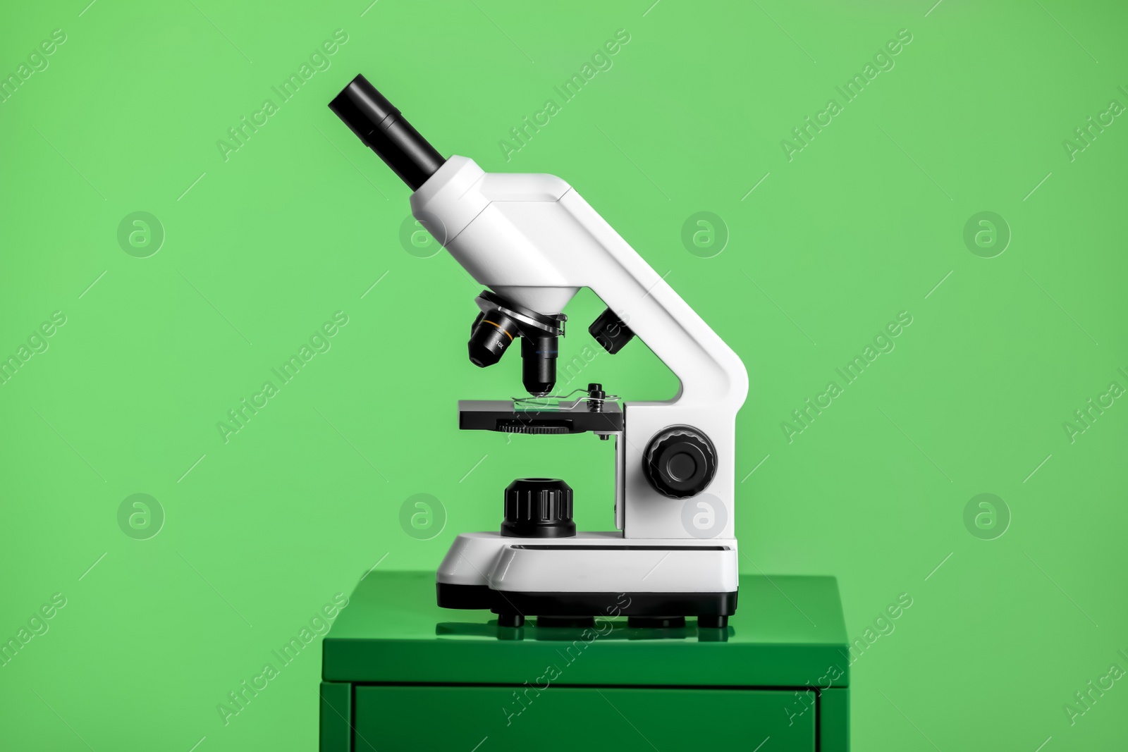 Photo of Modern medical microscope on lab drawer against green background