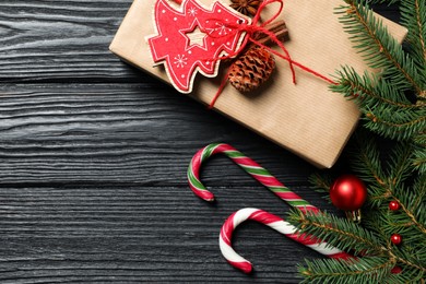 Photo of Gift box, candy canes, fir tree branches and Christmas decor on black wooden table, flat lay. Space for text