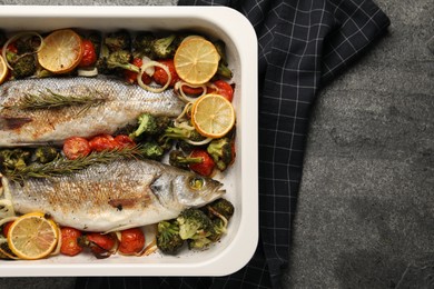 Delicious fish with vegetables and lemon in baking dish on grey textured table, top view. Space for text