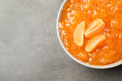 Photo of Tasty tangerine jam in bowl on grey table, top view. Space for text