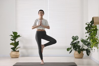 Girl practicing tree asana on mat in yoga studio. Vrksasana pose