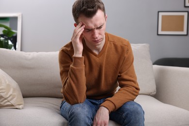 Photo of Sad man suffering from headache on sofa indoors