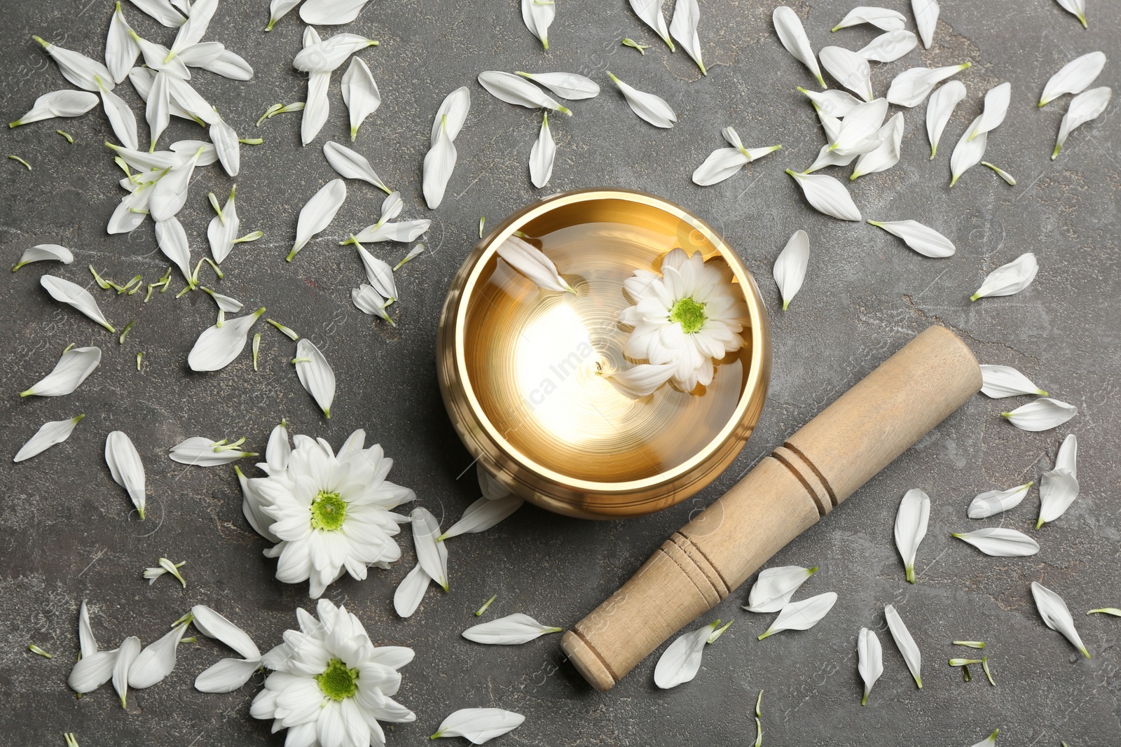 Photo of Golden singing bowl with flower and mallet on grey table, flat lay. Sound healing