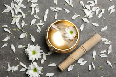 Golden singing bowl with flower and mallet on grey table, flat lay. Sound healing