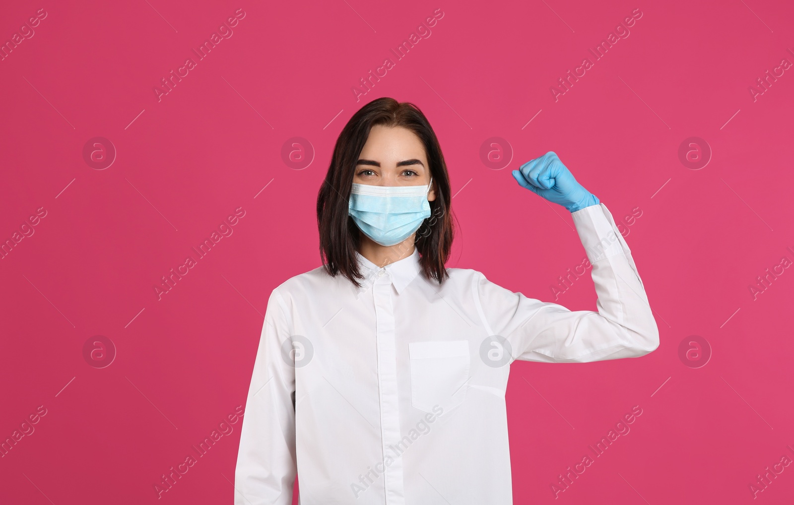 Photo of Woman with protective mask and gloves showing muscles on pink background. Strong immunity concept