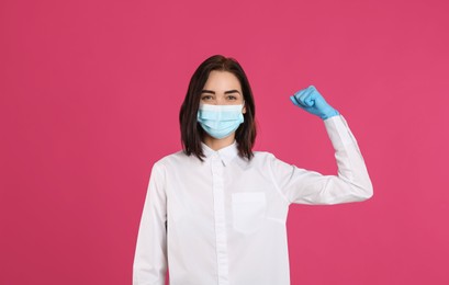 Woman with protective mask and gloves showing muscles on pink background. Strong immunity concept