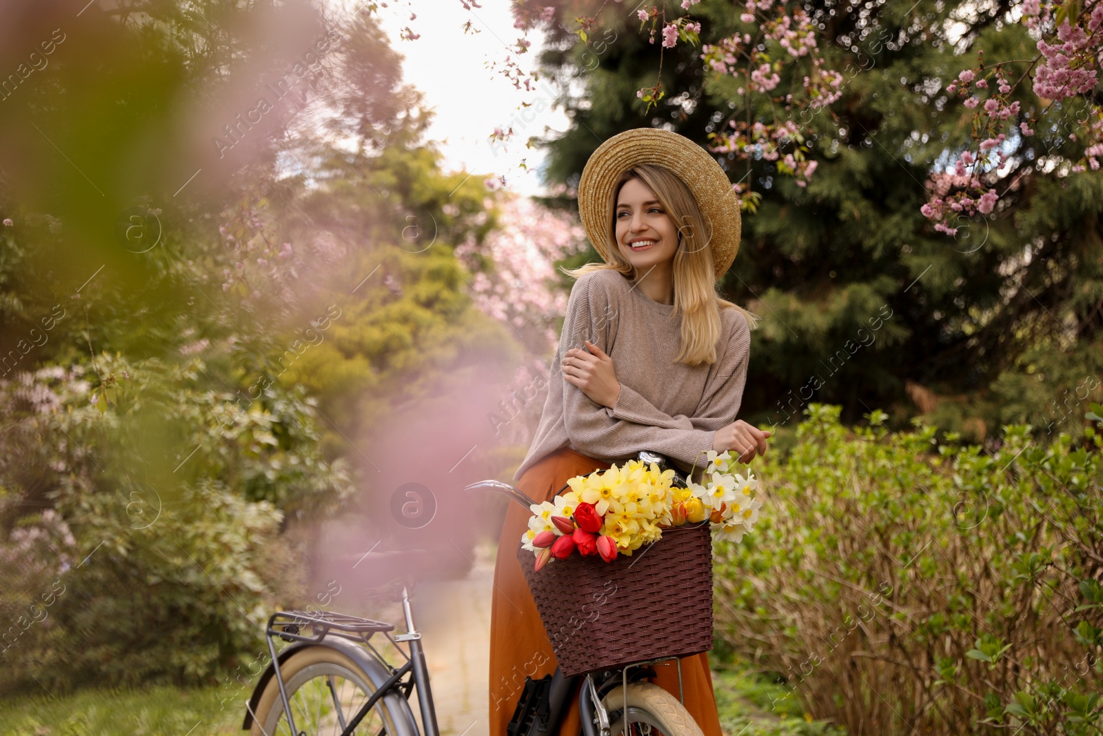 Photo of Beautiful young woman with bicycle and flowers in park on pleasant spring day. Space for text