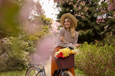 Photo of Beautiful young woman with bicycle and flowers in park on pleasant spring day. Space for text