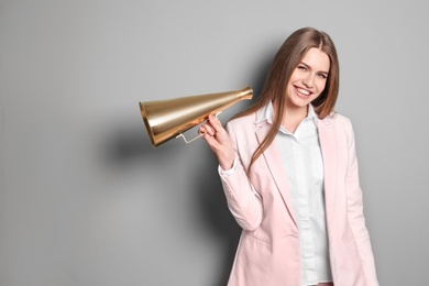 Young woman with megaphone on grey background