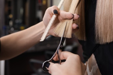 Photo of Professional hairdresser cutting woman's hair in salon, closeup