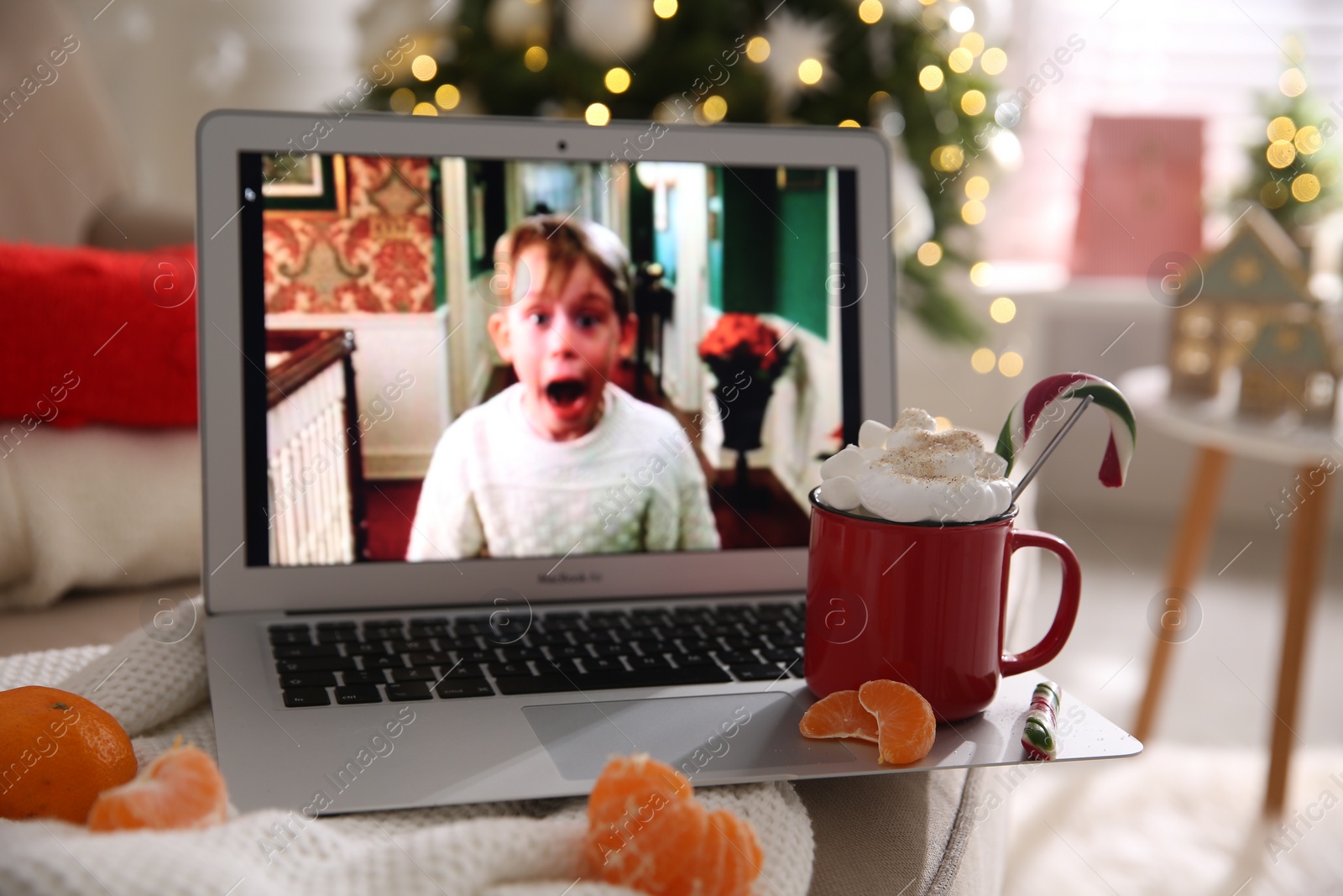 Photo of MYKOLAIV, UKRAINE - DECEMBER 25, 2020: Laptop displaying Home Alone movie indoors, focus on cup of sweet drink and tangerine slices. Cozy winter holidays atmosphere