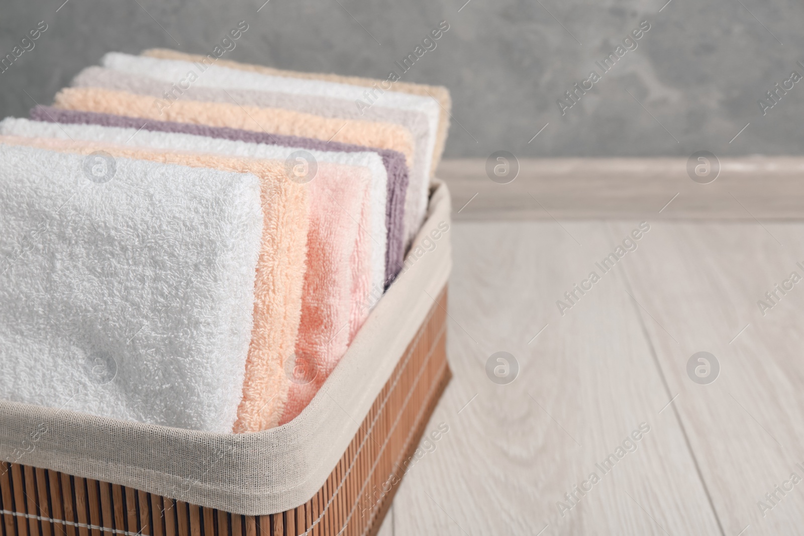 Photo of Laundry basket with clean terry towels on floor near grey wall