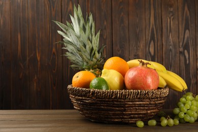 Wicker bowl with different ripe fruits on wooden table. Space for text