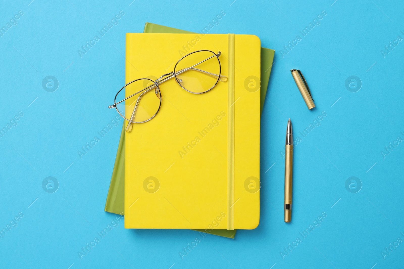 Photo of Ballpoint pen, notebooks and glasses on light blue background, flat lay