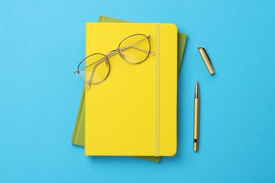 Photo of Ballpoint pen, notebooks and glasses on light blue background, flat lay
