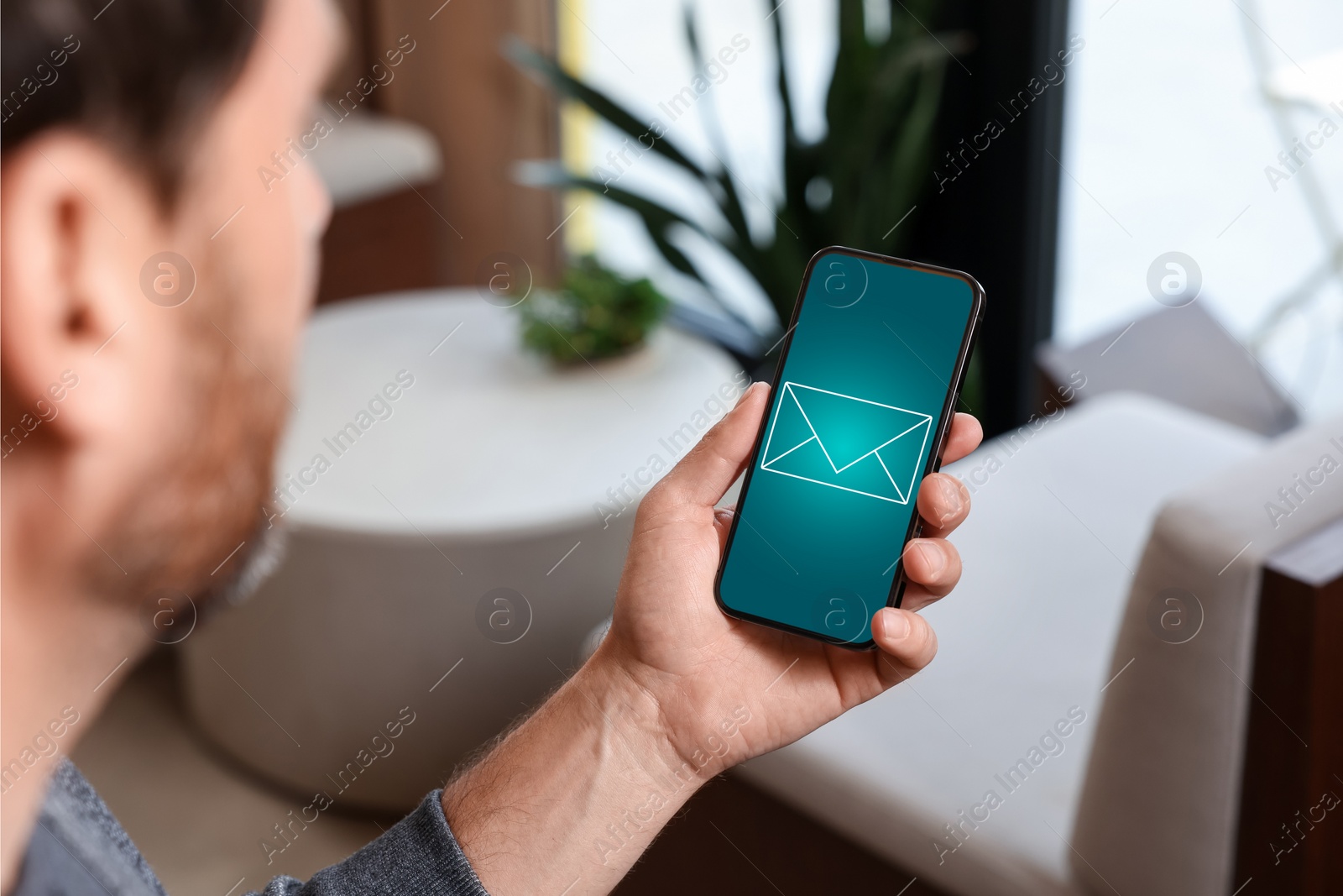Image of Man received message on mobile phone indoors, closeup. Envelope illustration on device screen