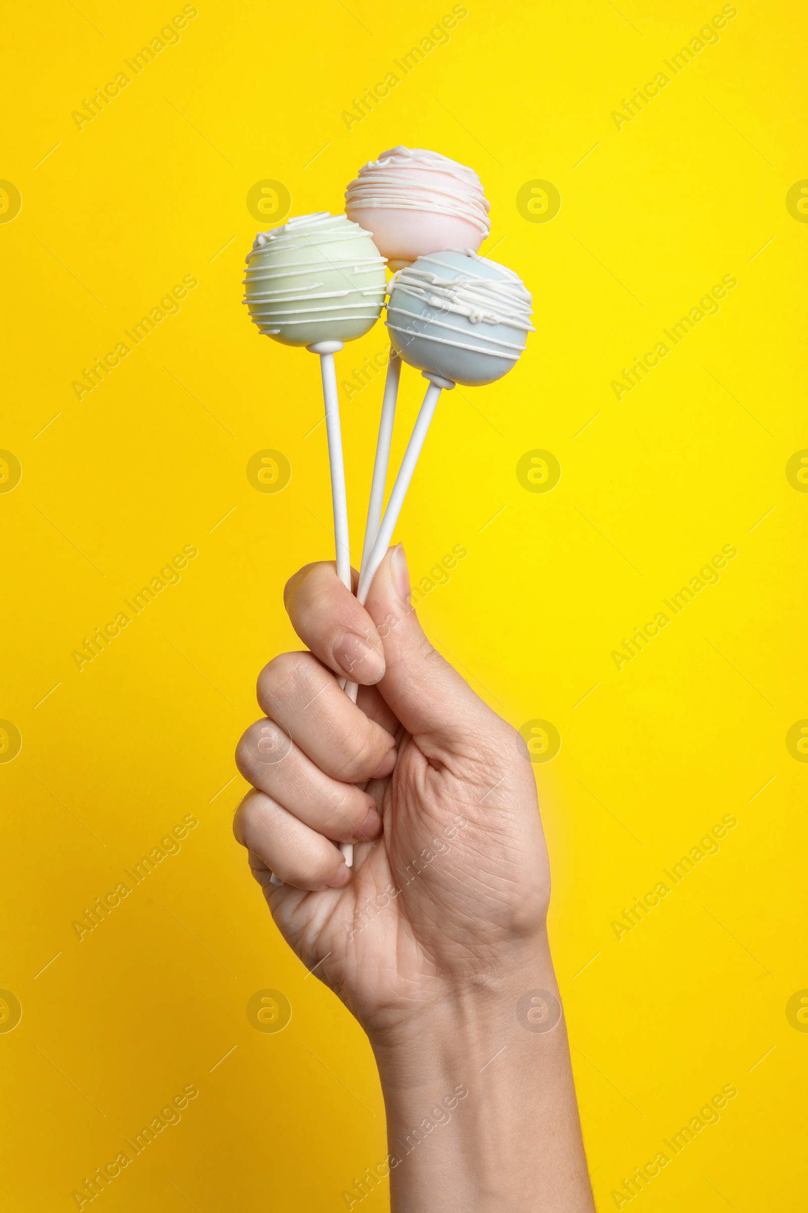 Photo of Woman holding sweet cake pops on yellow background, closeup