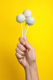 Woman holding sweet cake pops on yellow background, closeup