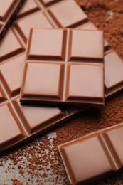 Delicious milk chocolate and cocoa powder on table, closeup