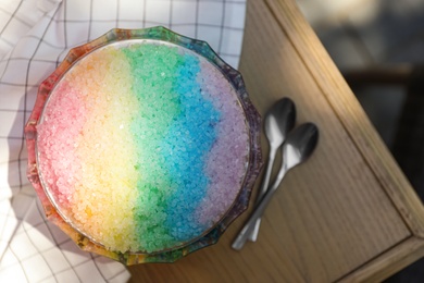 Rainbow shaving ice in glass dessert bowl and spoons on wooden table, flat lay