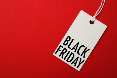 Image of White tag with phrase BLACK FRIDAY on red background, top view. Space for text