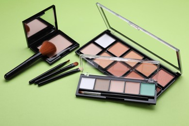 Photo of Colorful contouring palettes with brushes on light green background. Professional cosmetic product