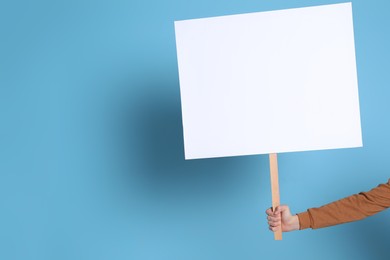 Woman holding blank sign on light blue background, closeup. Space for text