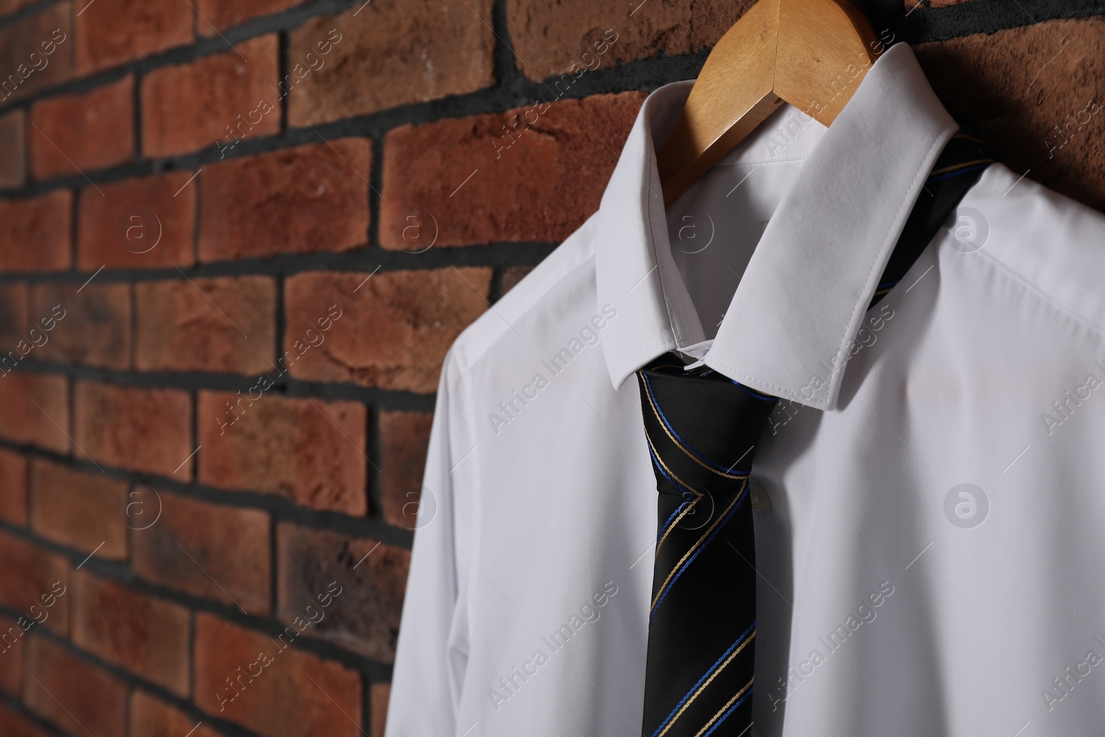 Photo of Hanger with white shirt and striped necktie on red brick wall, closeup. Space for text