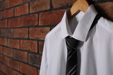 Hanger with white shirt and striped necktie on red brick wall, closeup. Space for text