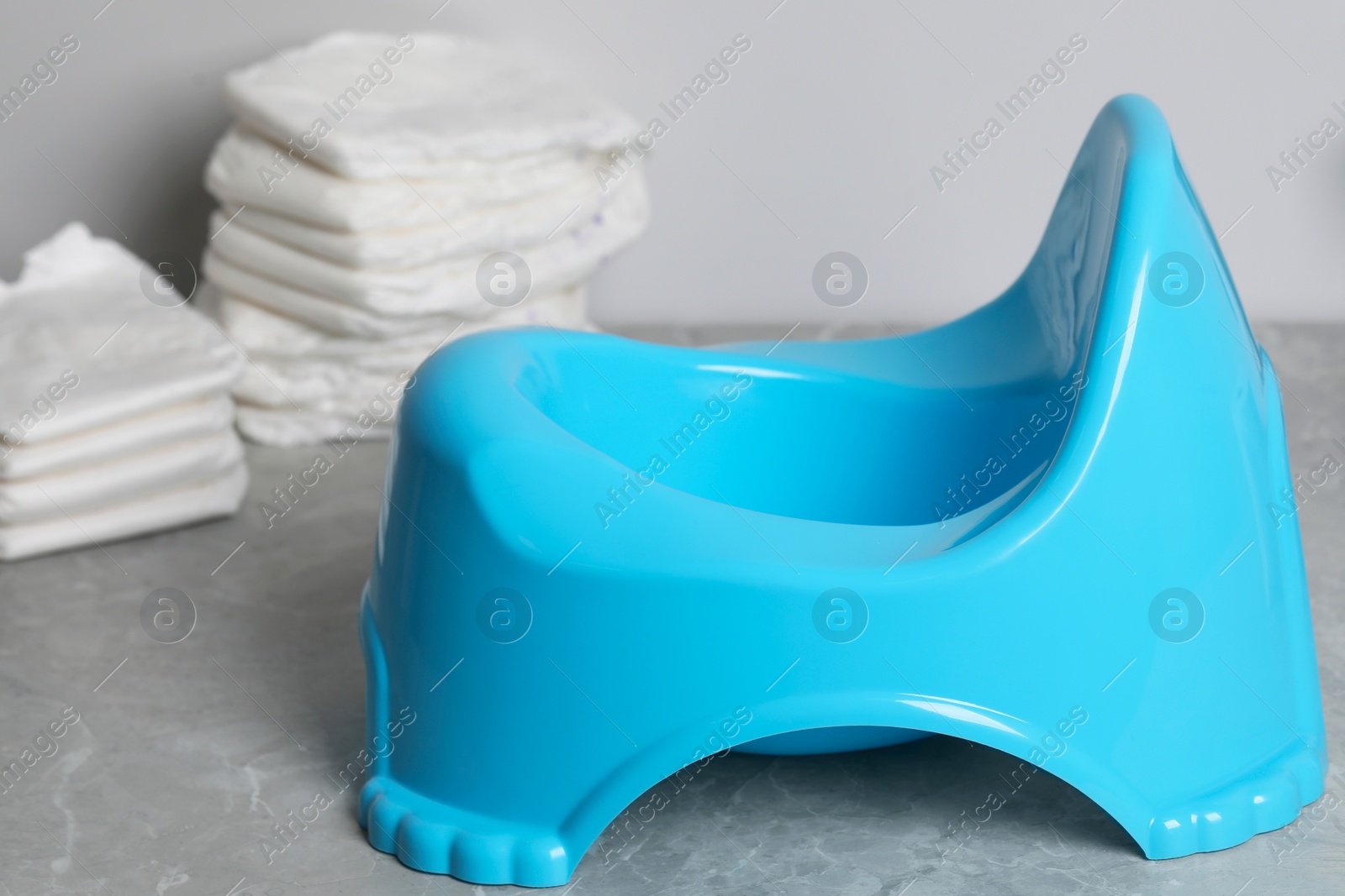 Photo of Light blue baby potty and diapers on grey table, closeup. Toilet training