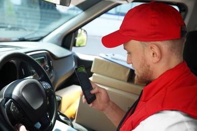 Photo of Young courier with smartphone and parcels in delivery car