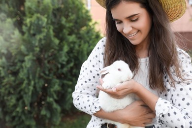 Photo of Happy woman with cute rabbit outdoors on sunny day. Space for text