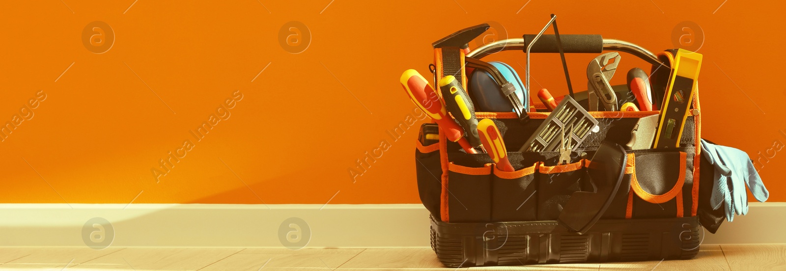 Image of Bag with different tools for repair on floor near orange wall, space for text. Banner design