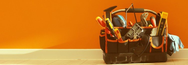 Image of Bag with different tools for repair on floor near orange wall, space for text. Banner design