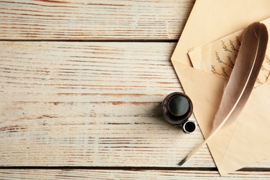 Photo of Feather pen, bottle of ink and letter on white wooden table, flat lay. Space for text