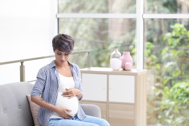 Trendy pregnant woman with tattoo on sofa indoors