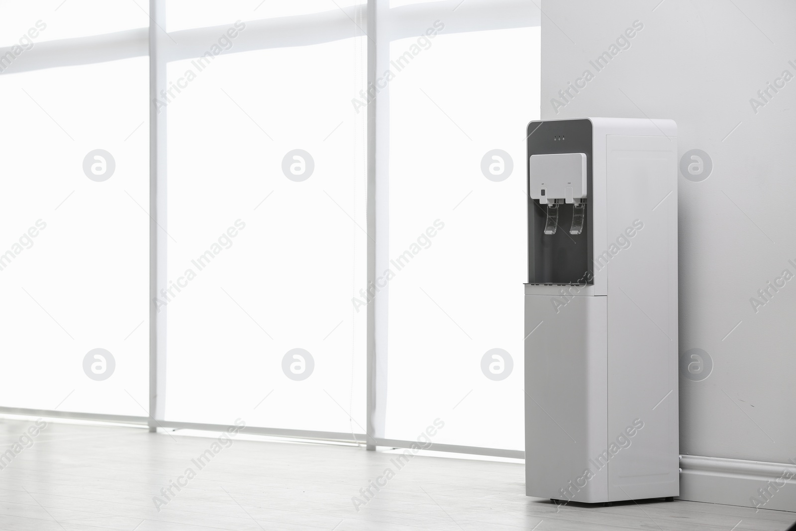 Photo of Modern water cooler near white wall indoors. Space for text