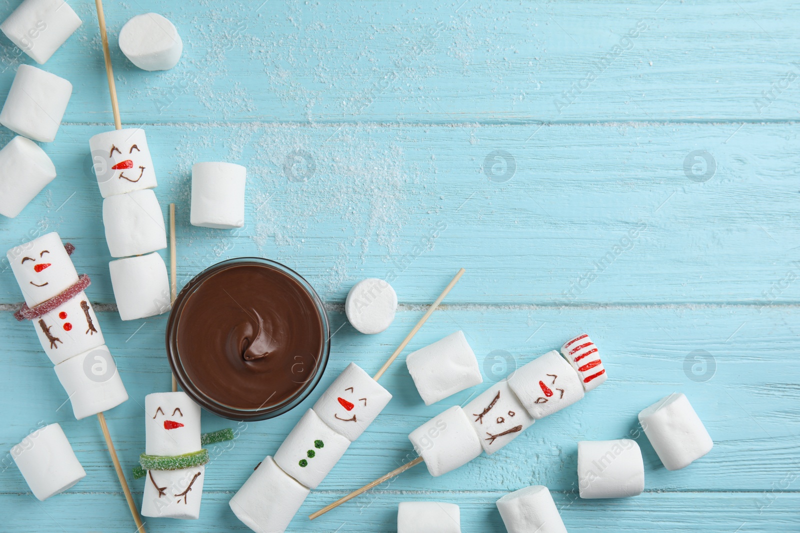 Photo of Snowmen made of marshmallows and chocolate paste on light blue wooden background, flat lay. Space for text