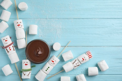 Snowmen made of marshmallows and chocolate paste on light blue wooden background, flat lay. Space for text