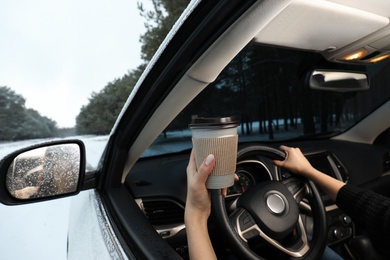 Young woman with coffee driving car along winter forest, closeup