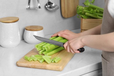 Photo of Woman cutting fresh green celery at white table, closeup