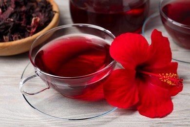 Photo of Delicious hibiscus tea and beautiful flower on light wooden table, closeup