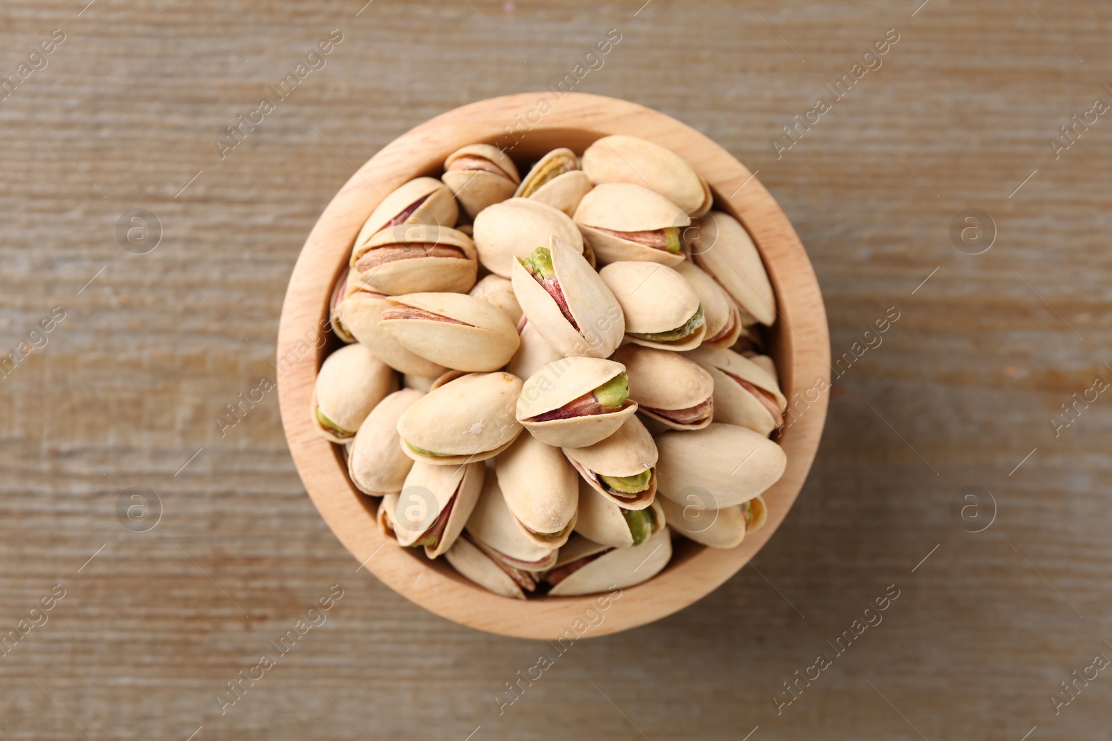 Photo of Tasty pistachios in bowl on wooden table, top view